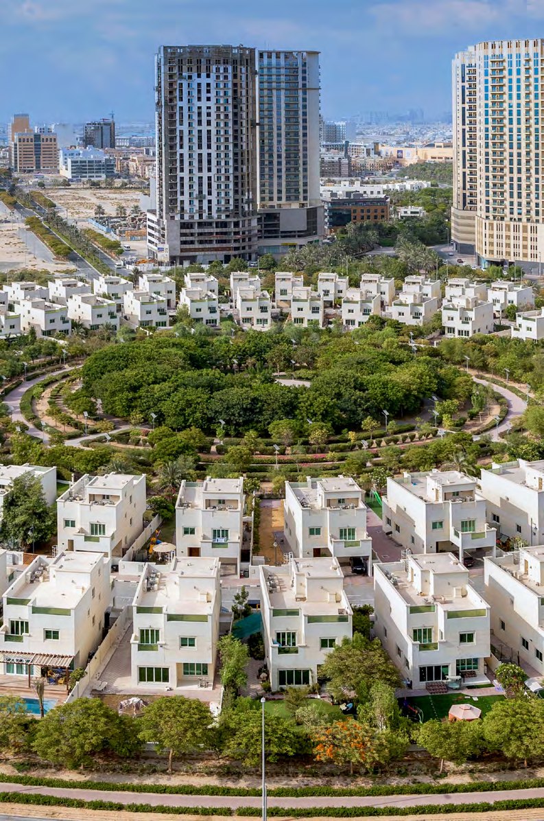 Aerial view of Jumeirah Village Circle: villas around the community park with residential towers beyond