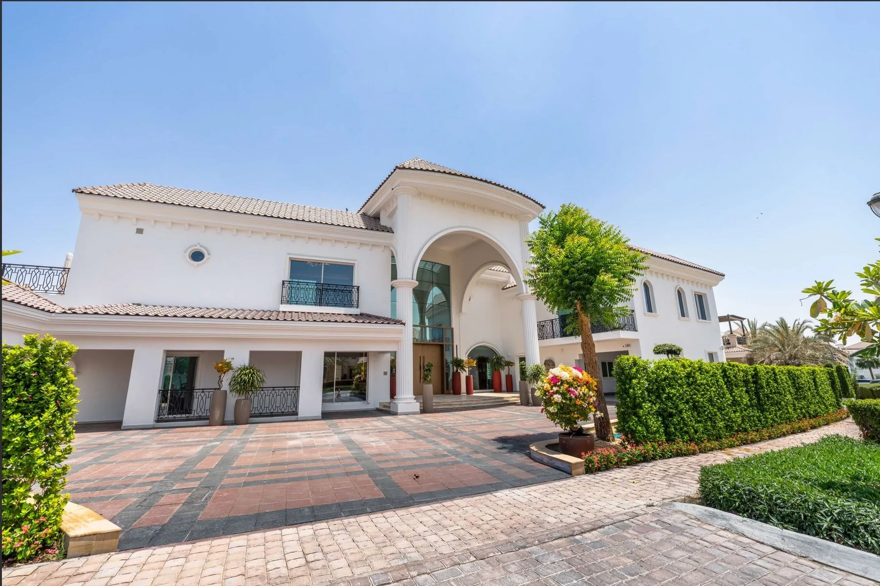 The front of the mansion from the driveway — arched portico, palm trees and clipped hedges