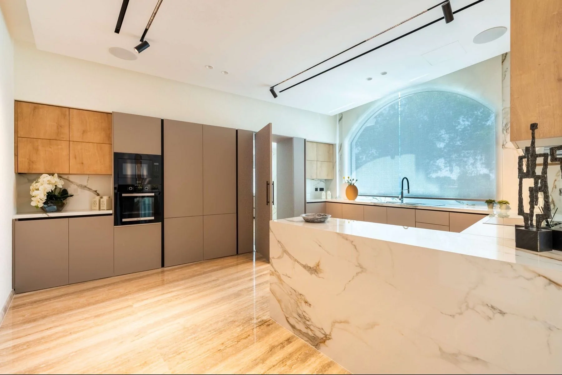 The kitchen with a marble island, branded built-in appliances and an arched window